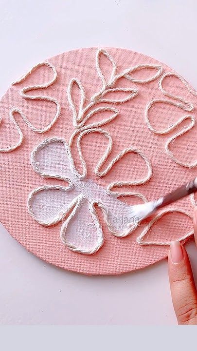 Embossed floral art in progress on a pink canvas with a white paintbrush, highlighting textured petals and leaves.