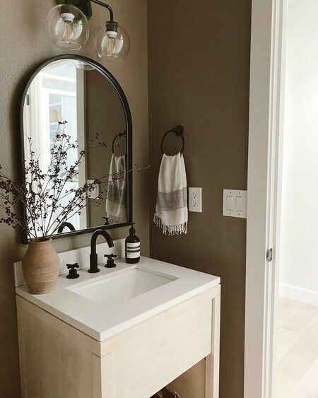 Modern bathroom vanity with oval mirror, brown decor, and potted plant for a stylish, minimalist look.