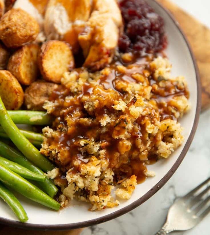 Delicious holiday meal with stuffing, green beans, roasted potatoes, and cranberry sauce on a plate, topped with rich gravy.