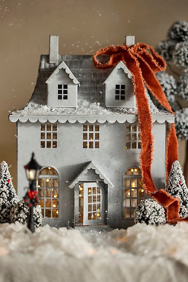 Miniature winter scene with a charming house, orange ribbon, and snowy trees, illuminated by warm lights for a festive feel.