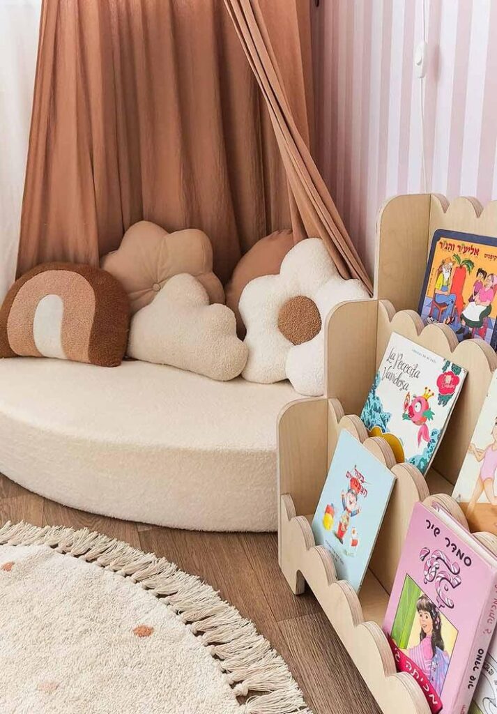 Cozy kids' reading nook with soft cushions, books on a wooden shelf, and a round rug in a playroom with pastel decor.