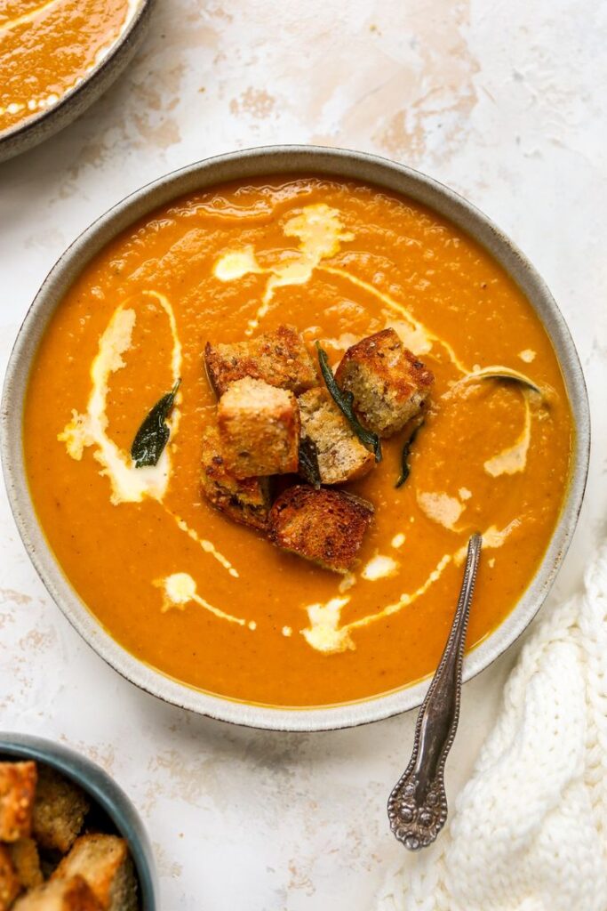 Creamy pumpkin soup with croutons and herbs in a bowl, perfect for a cozy autumn meal.