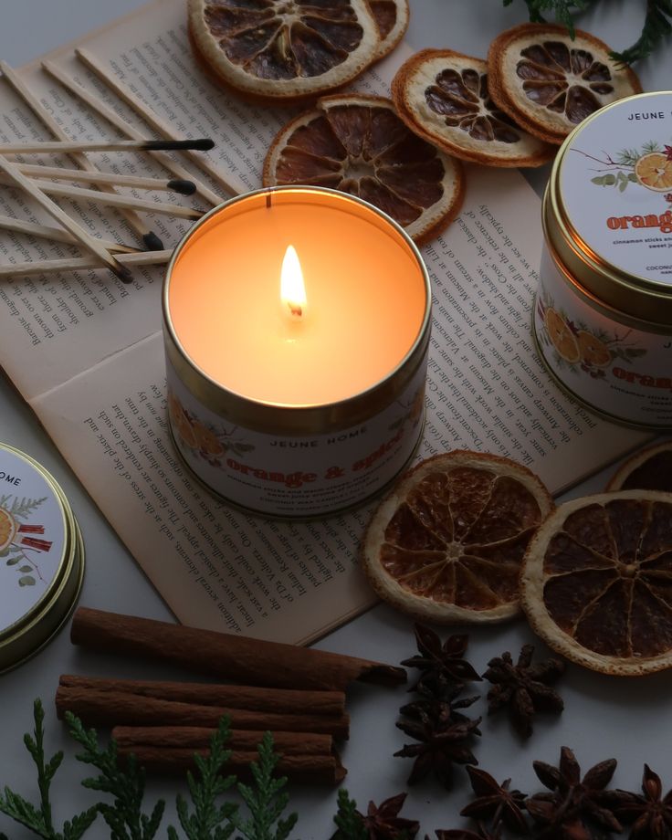 Cozy scene with lit orange-spice candle, dried citrus slices, cinnamon sticks, and a book. Perfect for relaxation and aromatherapy.