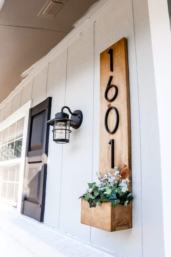 House number 1601 decor on wood with flower box beneath and a wall-mounted lantern against a white siding in daylight.