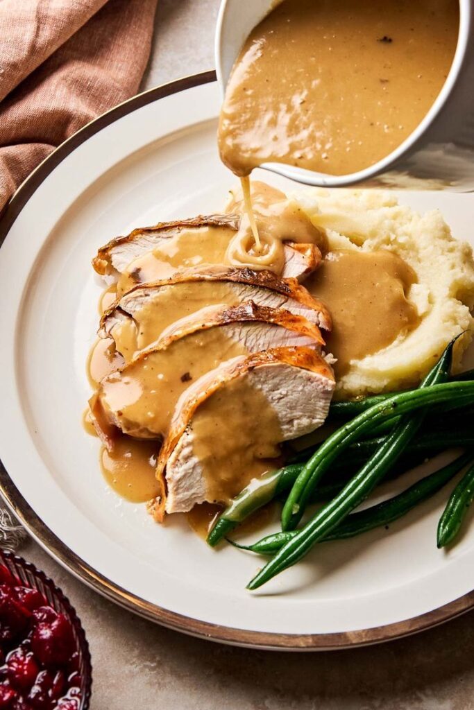 Sliced turkey breast with gravy, mashed potatoes, and green beans on a plate. Perfect holiday meal or Thanksgiving dinner.
