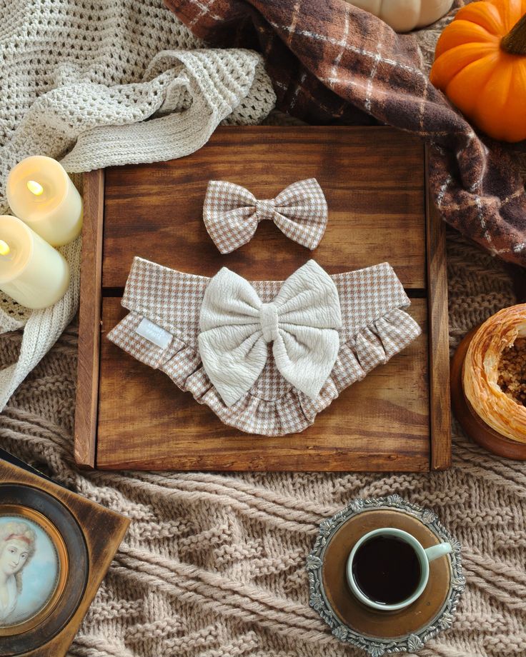 Cozy autumn setup with checked bow ties and candles on a wooden tray, surrounded by knit blankets and pumpkins.