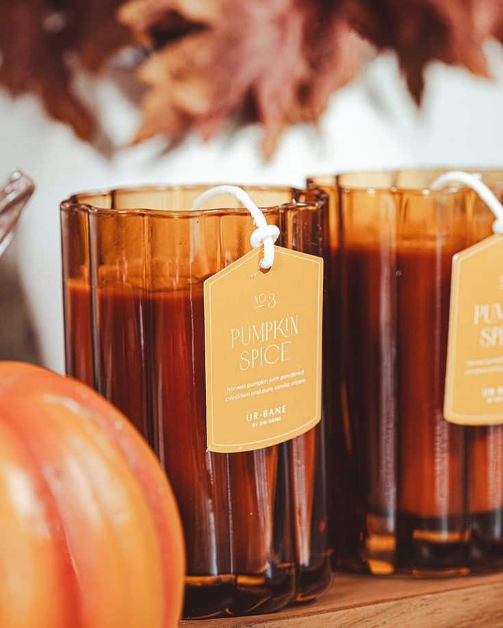 Pumpkin spice candle with orange glass jar, autumn leaves, and decorative pumpkins, perfect for cozy fall ambiance.