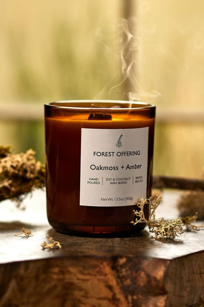Aromatic Oakmoss and Amber candle in a glass jar, emitting smoke, on a rustic wooden surface with moss accents.