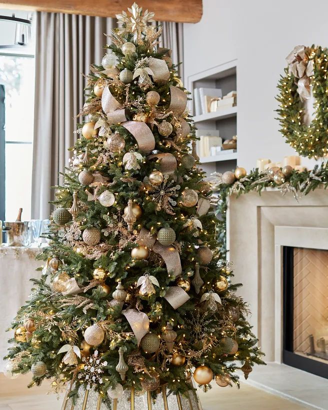 Elegant Christmas tree with gold and silver ornaments, ribbons, and lights in a cozy living room setting.