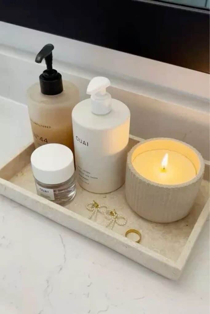 Luxurious bathroom essentials on a tray: skincare, OUAI products, and a lit candle for a calming ambiance. Perfect self-care setup.