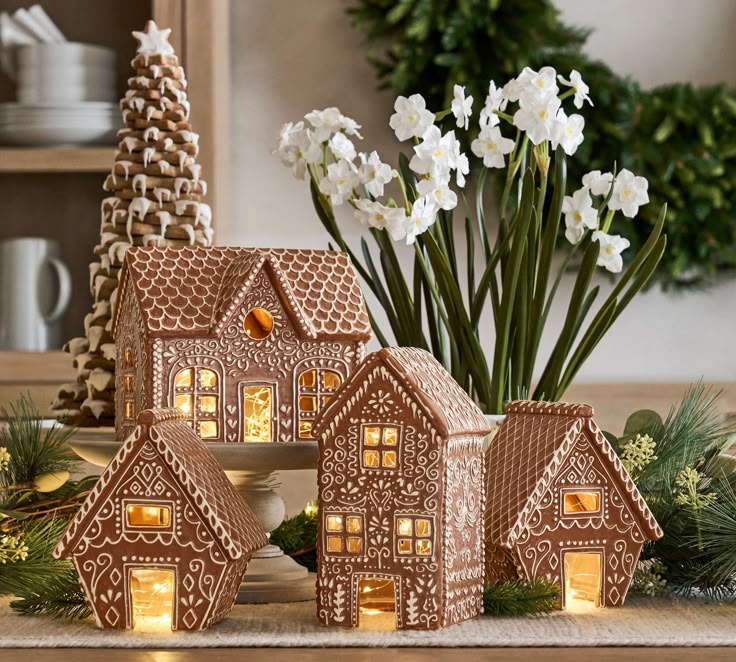 Gingerbread houses with intricate icing designs lit from within, surrounded by flowers and festive greenery. Perfect for holiday decor.