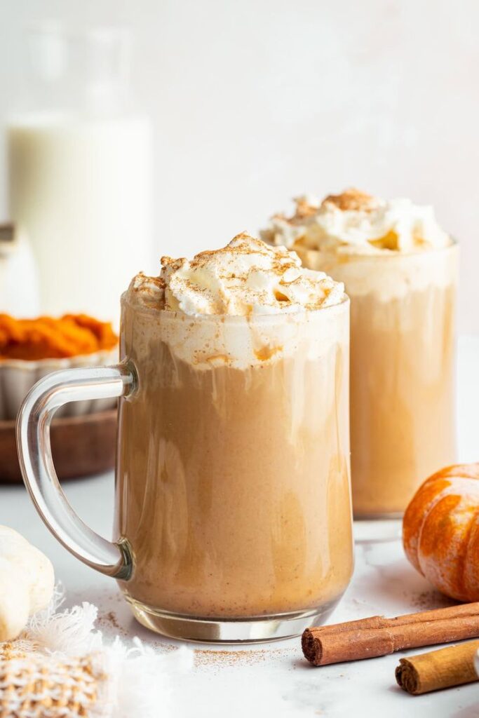 Pumpkin spice latte with whipped cream in glass mugs, surrounded by cinnamon sticks and pumpkins. Perfect for autumn vibes.