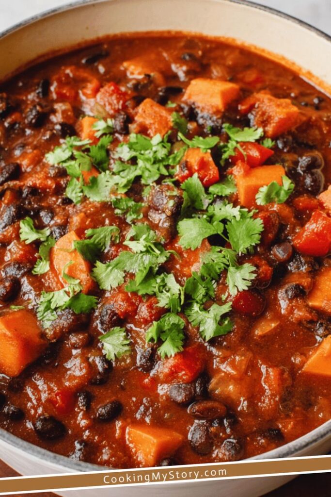 Hearty black bean chili with sweet potatoes and cilantro garnish, perfect for a cozy meal, in a pot.