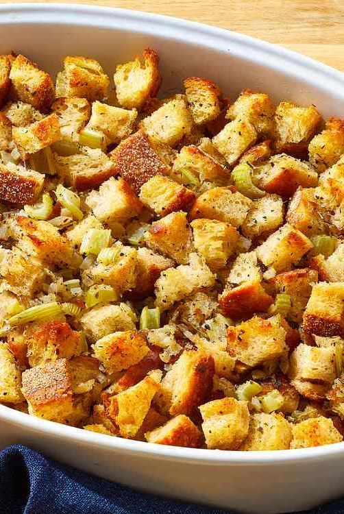 Delicious homemade stuffing with golden-brown bread cubes and celery in a white baking dish—perfect for Thanksgiving dinner.