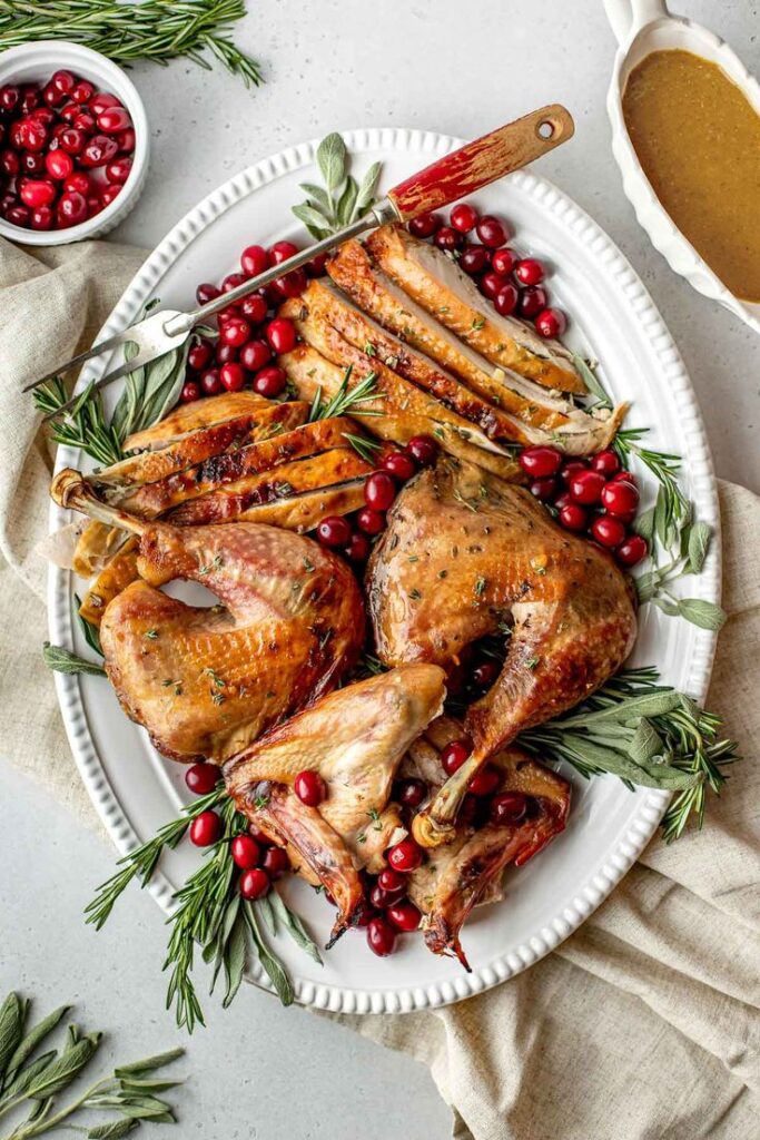 Roast turkey with herbs and fresh cranberries on a white platter, served with gravy for a festive holiday meal.