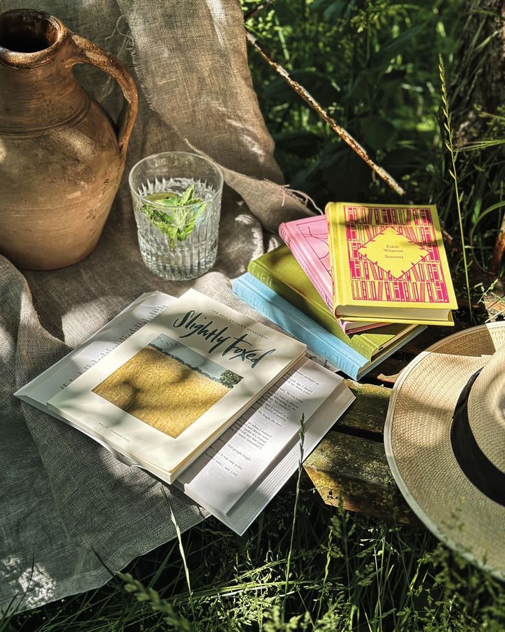 Books and straw hat on picnic with a jug and mint water, set on grass for peaceful afternoon reading.