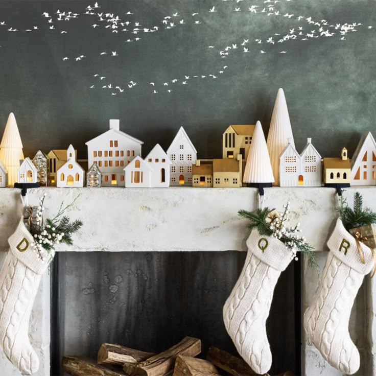 Cozy Christmas mantel with stockings and decorative village scene, accented by a flock of birds on a chalkboard wall.