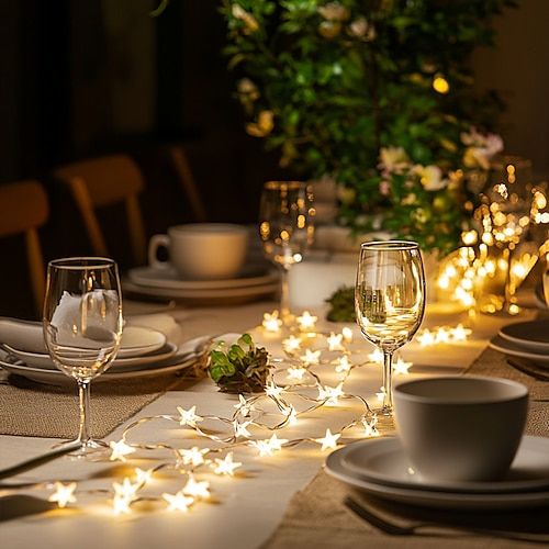 Elegant dinner table with star-shaped string lights, wine glasses, and greenery, creating a warm, inviting atmosphere for a night gathering.
