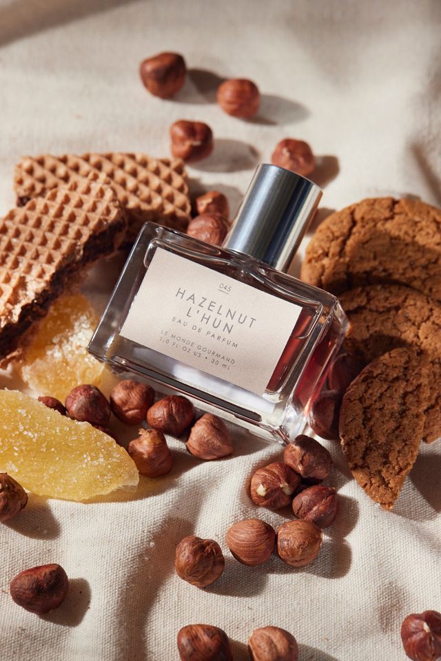 Perfume bottle on linen with hazelnuts, wafers, and ginger treats, evoking a rich, aromatic gourmand scent.