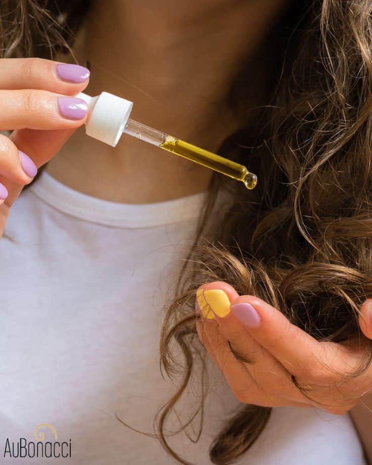 Applying hair oil with dropper to curly hair for nourishment. Ideal for hair care routine and maintaining healthy, shiny locks.