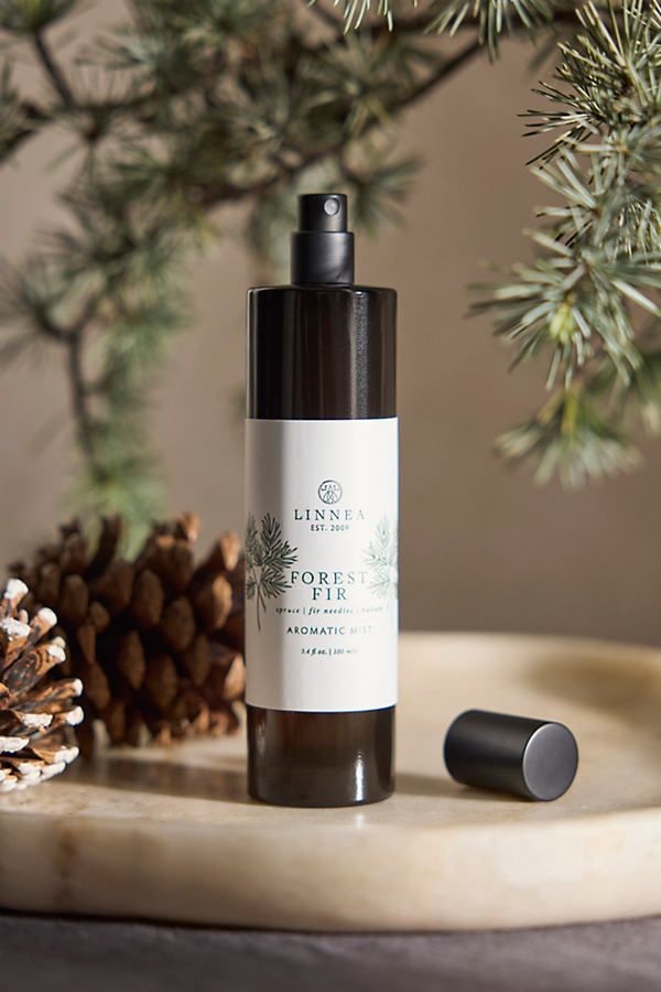 Forest-themed aromatic spray bottle on a marble surface with pine cones and branches; Linnea Forest Fir scent.