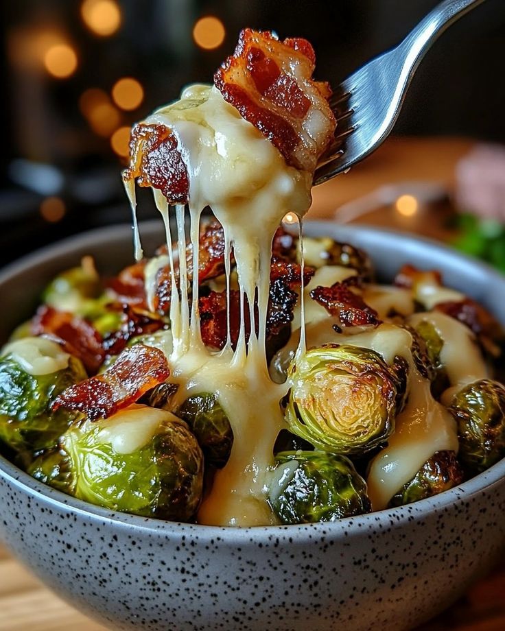 Cheesy bacon Brussels sprouts in a bowl, with fork pulling melted cheese for a savory, delicious side dish.