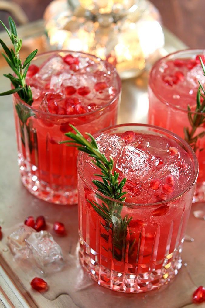 Chilled pomegranate cocktails garnished with rosemary, served in clear glasses, perfect for festive gatherings.