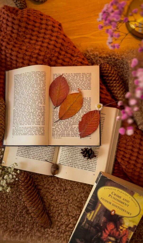 Cozy autumn reading scene with open books, dried leaves, pine cones, and Crime and Punishment by Fyodor Dostoyevsky.