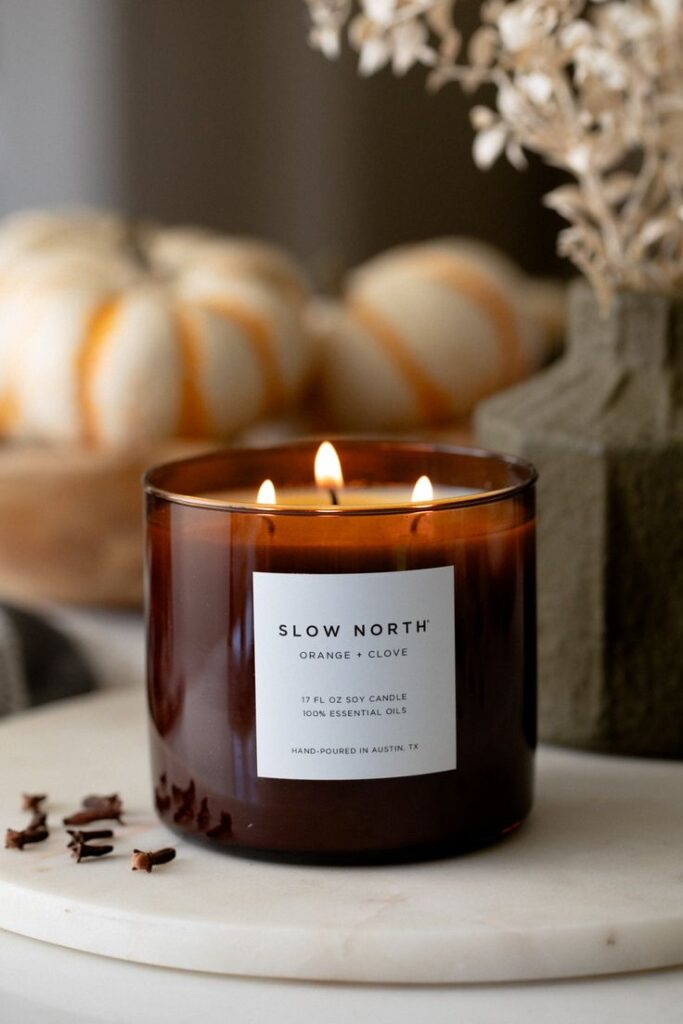 Lit soy candle with orange and clove scent, surrounded by pumpkins and dried flowers, creating a cozy autumn ambiance.