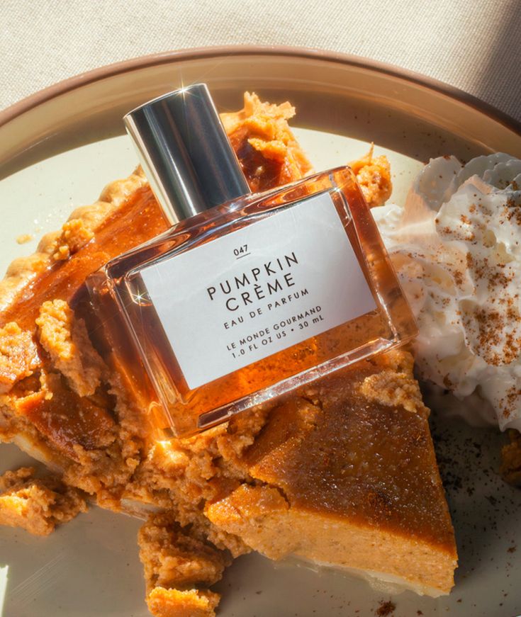 Perfume bottle labeled Pumpkin Crème on a plate with pumpkin pie and whipped cream, evoking a cozy fall vibe.