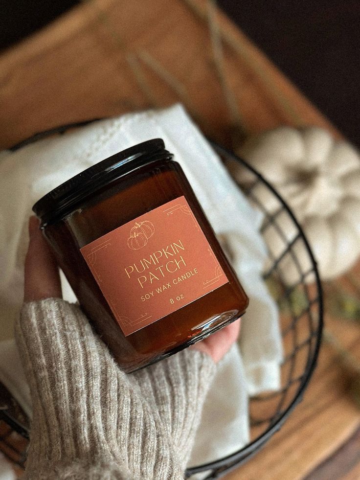 Cozy autumn vibe with a hand holding a Pumpkin Patch soy wax candle in a warm-toned setting with a knit sleeve.