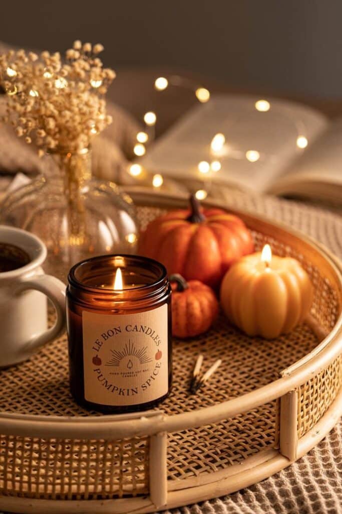 Cozy fall scene with pumpkin spice candle, pumpkins, and fairy lights on a tray, creating a warm autumn ambiance.