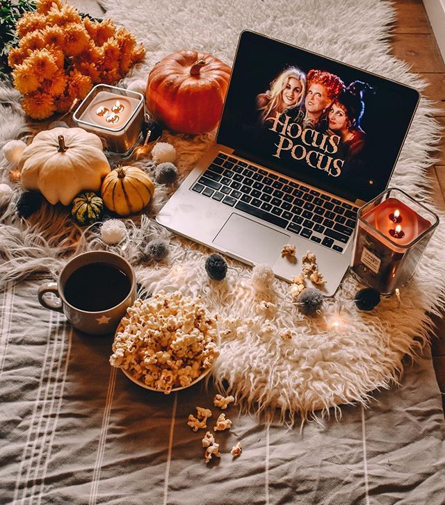 Cozy autumn setup with a laptop playing Hocus Pocus, surrounded by pumpkins, popcorn, candles, and a cup of coffee.