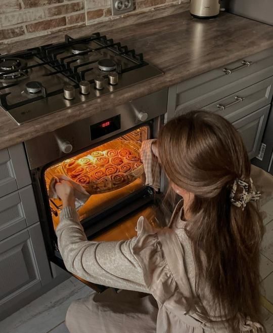 Woman baking fresh cinnamon rolls in a modern kitchen oven, showcasing a cozy home baking scene.