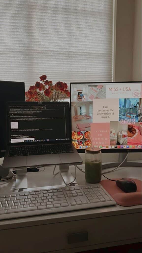 Home office setup with dual monitors, laptop, keyboard, flowers, and a green smoothie, creating a productive workspace ambiance.