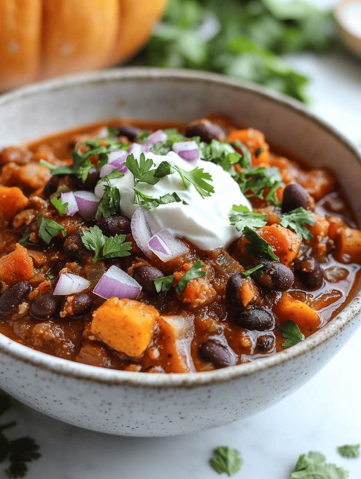 Hearty bowl of pumpkin chili topped with sour cream, red onions, and cilantro. Perfect fall comfort food in a rustic bowl.