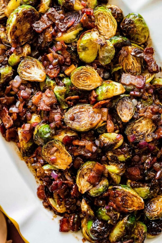 Roasted Brussels sprouts with crispy bacon and red onions, served on a white platter, perfect for a savory side dish.