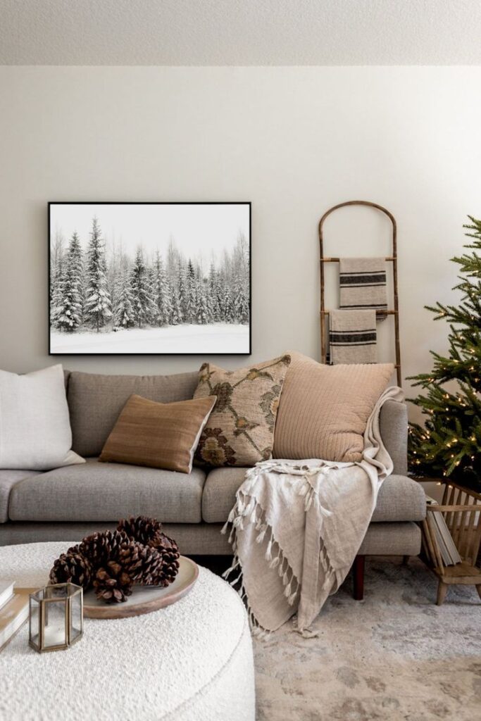 Cozy living room with neutral decor, gray sofa, textured cushions, and winter forest wall art. Warm, inviting holiday ambiance.