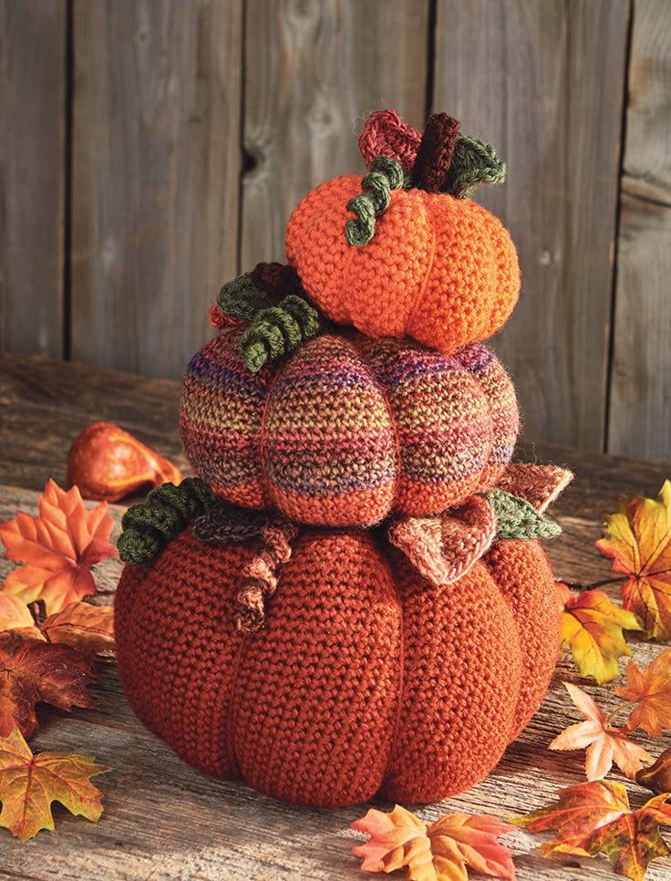 Crocheted stacked pumpkins with autumn leaves on wooden table, perfect for fall decor and cozy seasonal home styling.