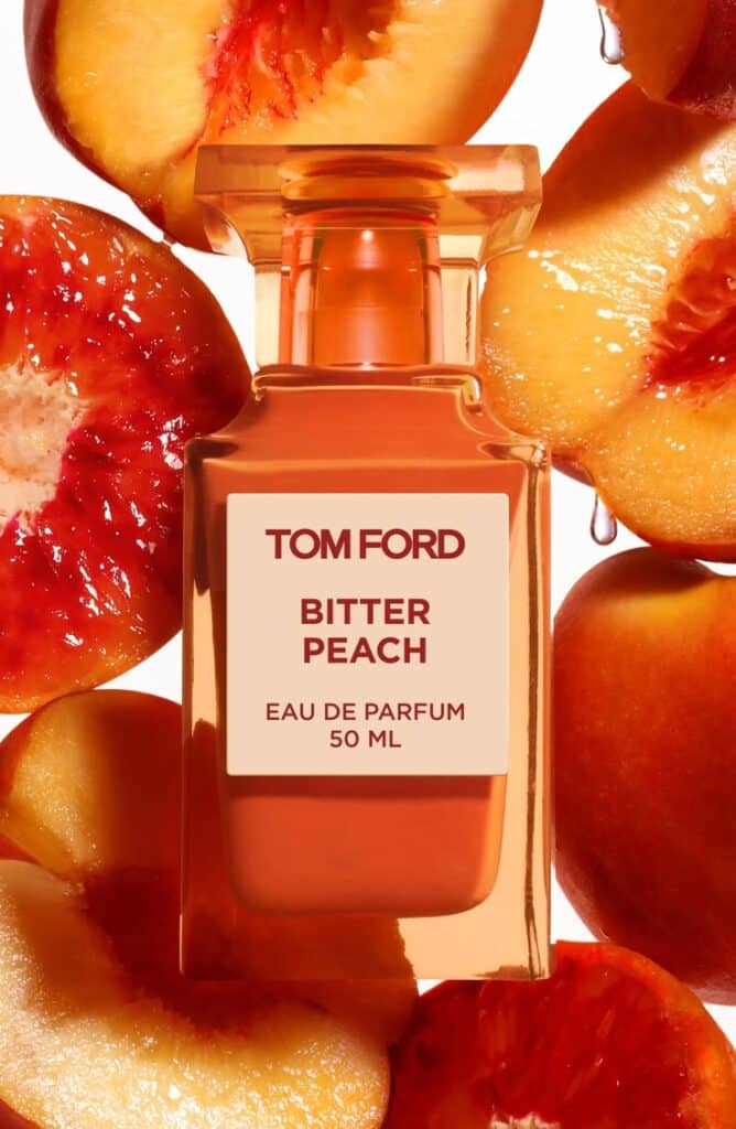 Tom Ford Bitter Peach Eau de Parfum bottle surrounded by sliced peaches, highlighting a vibrant, fruity fragrance essence.