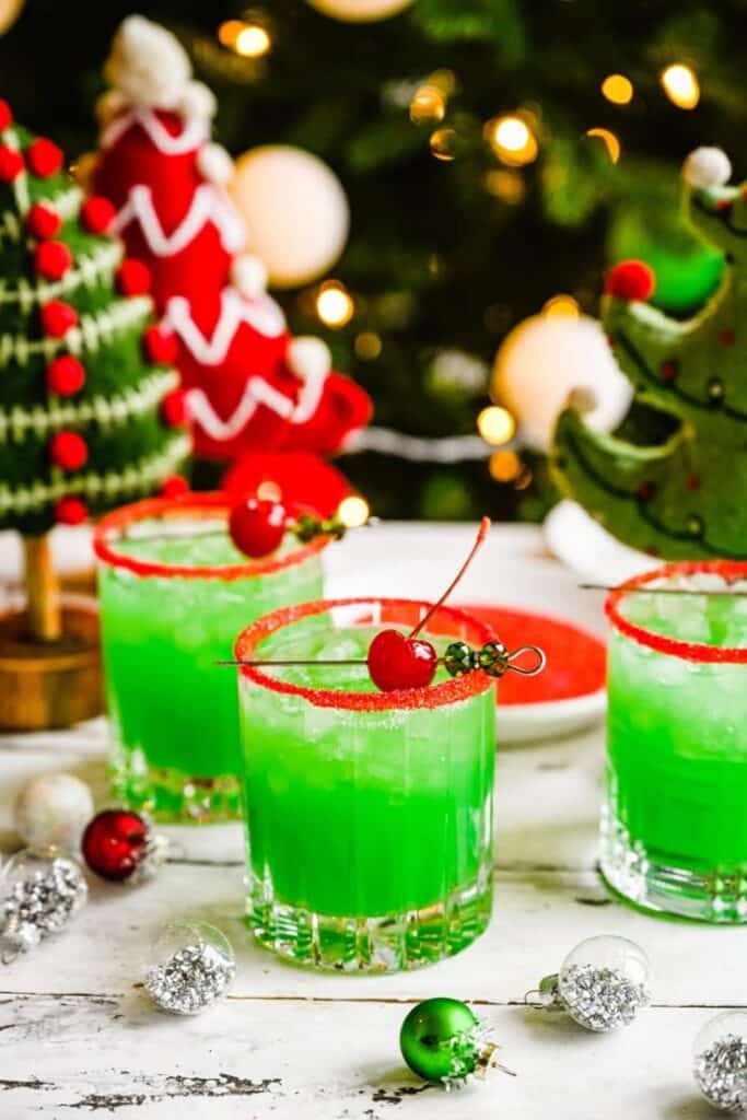 Festive green cocktails with cherries in holiday setting, garnished with red sugar rim, surrounded by Christmas décor.
