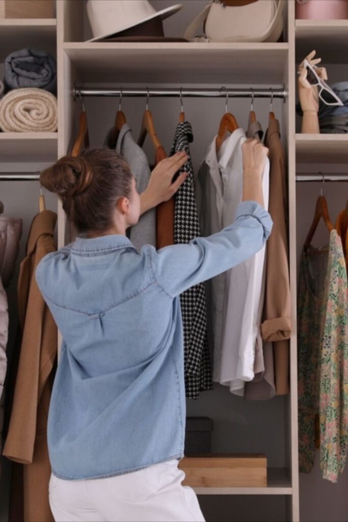 Woman organizes clothes in a neatly arranged closet, showcasing stylish garment options.