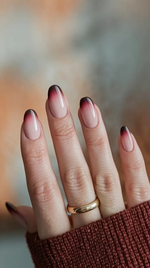 Gradient nail art with dark tips on manicured hand, wearing a gold ring and a cozy brown sweater.