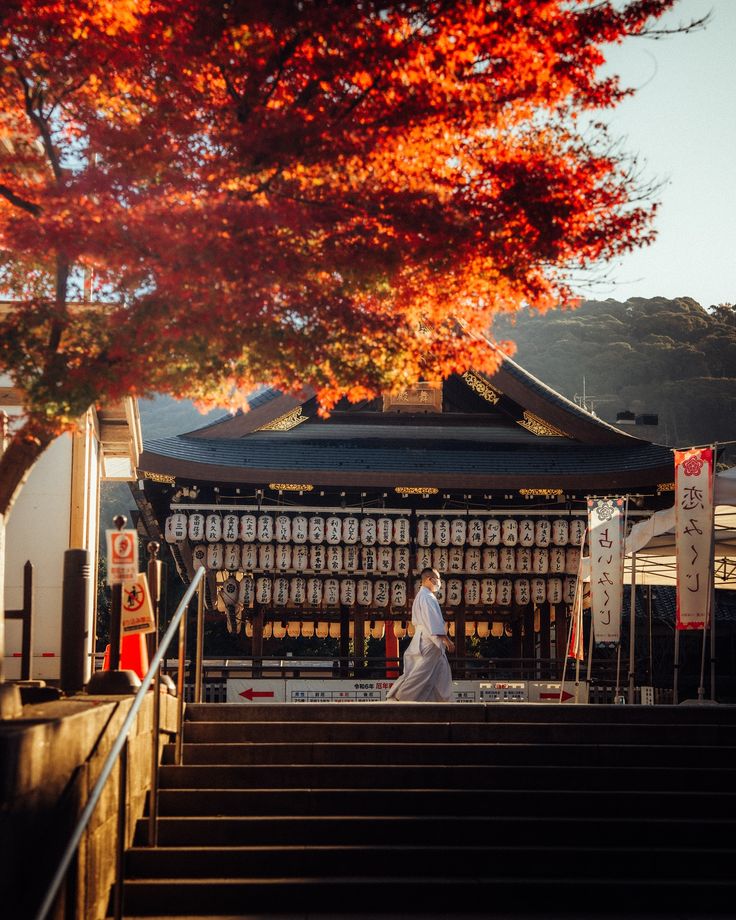 Japanese temple with a person in traditional attire, set under vibrant autumn leaves and lanterns.