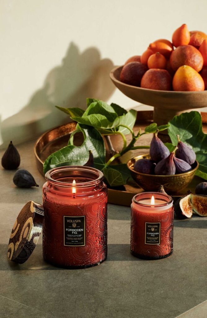 Elegant red candles with fig scent, next to fresh figs and a bowl of fruit, create a warm, inviting atmosphere.