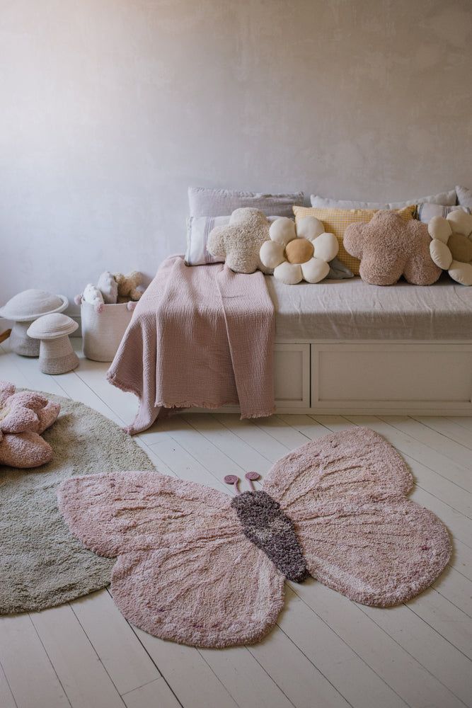 Cozy bedroom with butterfly rug, floral pillows, and soft pink accents, creating a serene and inviting atmosphere.