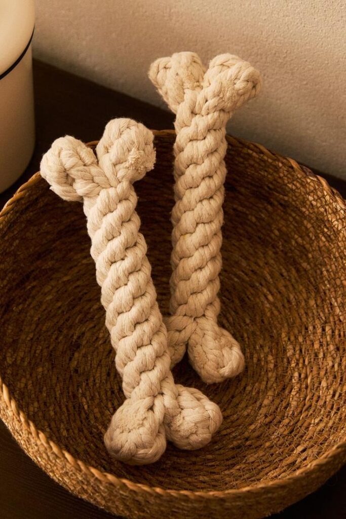 Two braided rope toys shaped like bones sit in a woven basket, perfect for pet playtime and decor.