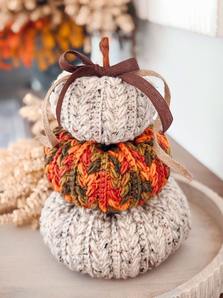 Hand-knitted pumpkins stacked as a decoration, featuring beige and orange yarn with bows, perfect for autumn decor.