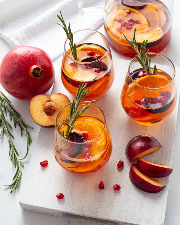 Refreshing fruit sangria with sliced peaches, pomegranate seeds, and rosemary on a wooden board, perfect for a summer gathering.