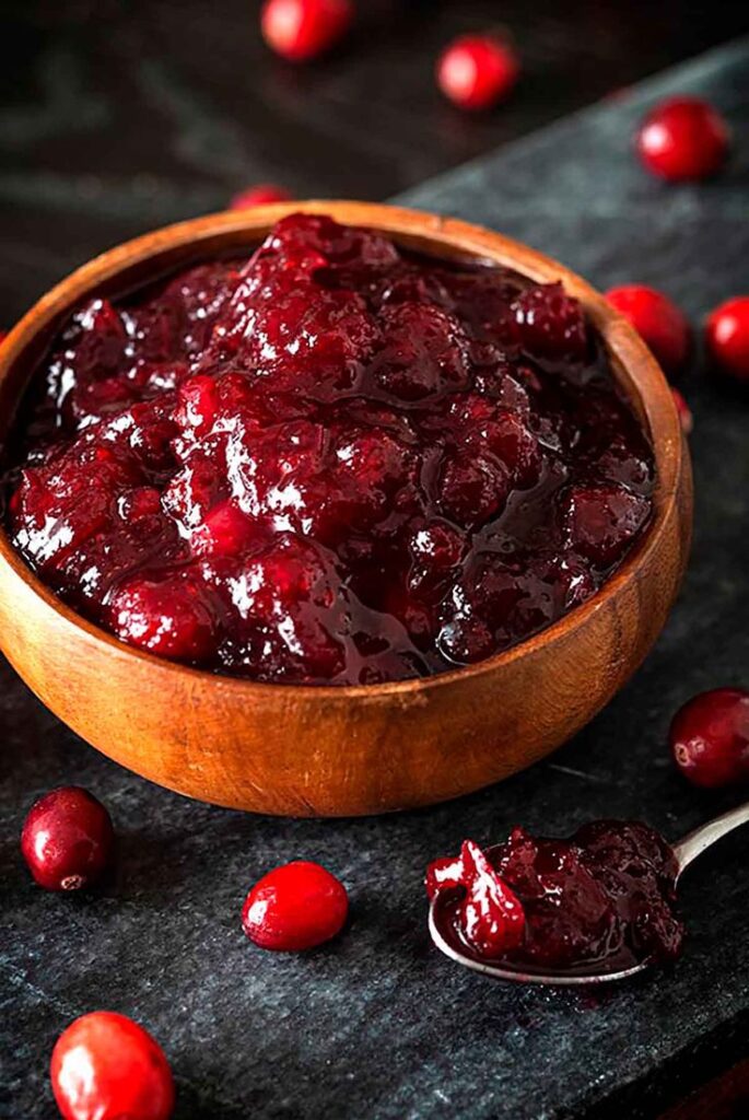 Rich homemade cranberry sauce in a wooden bowl, surrounded by fresh cranberries, perfect for festive meals.